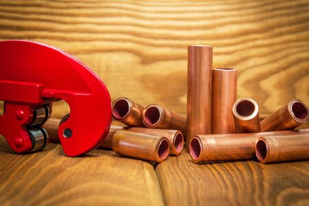 Copper pipes and red pipe cutter with connectors for plumbing repairs on vintage wooden boards close upの写真素材