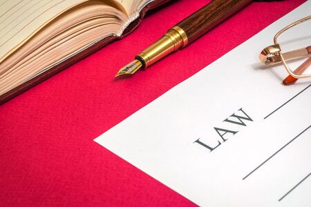 Office still life red table with notebook, gilded pen and Law on which glasses is preparing for the notesの写真素材