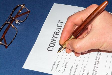 Businessman writes contract on blue table in the office or bank, hand holds a penの写真素材