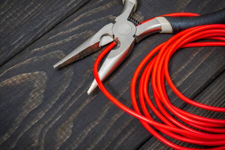 Electrician tool and red wire on black wooden boards for repairing energized systems or...