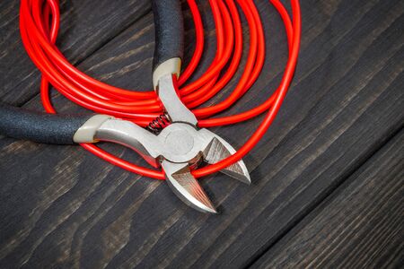 Electrician pliers and red wire on black wooden boards for repairing energized systems or communicationsの写真素材