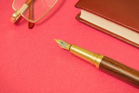 Office still life red table with notebook, gilt pen and glasses businessman prepare for notesの写真素材