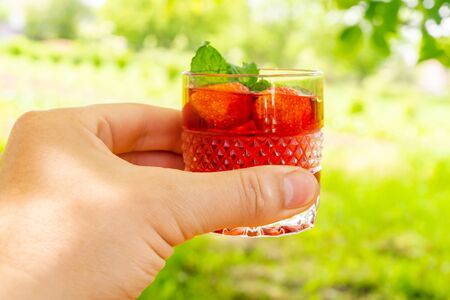 Hand holds glass with fresh strawberry and mint drink refreshing brisk summerの写真素材