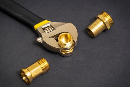 Plumbing brass fittings and adjustable spanner closeup on dark background during repair or replacement of spare partsの写真素材