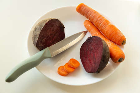 Cut carrots and beets with knife in a plate before cooking. Idea for dieting or fasting days