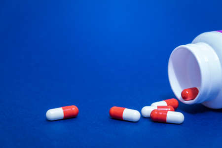 Red and white pill capsules poured from a white plastic bottle container. Global healthcare concept...