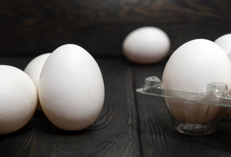 The white eggs are stacked in a tray and on black vintage boards. Egg sorting in chicken farm