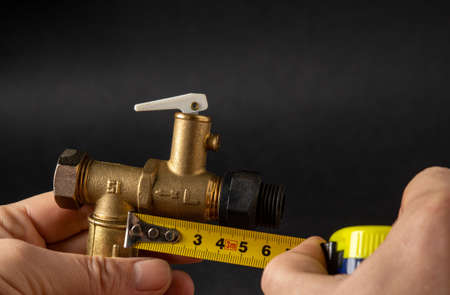 Closeup of a master measuring the size of a plumbing valve with a tape measureの写真素材