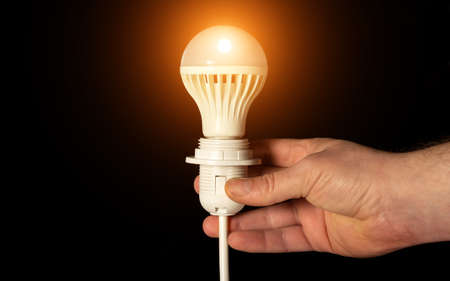 Close-up of hand holding a glowing light bulb on black background