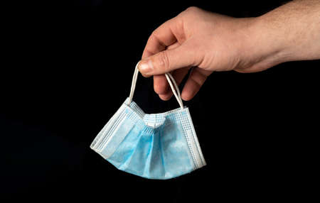 Hand holding a medical mask on an isolated black background to throw away. Quarantine closed