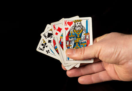 Person's hands are holding playing cards four kings close up on black background