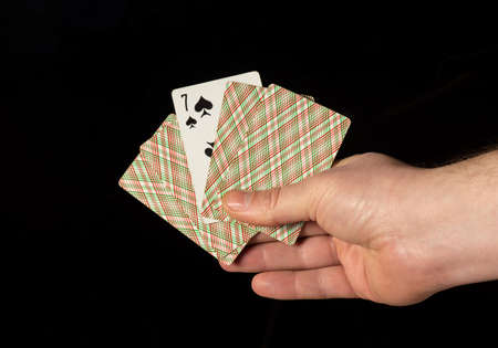 Person hands are holding playing cards and seven spades close up on black background
