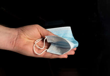 Hand holding a medical mask on an isolated black background to throw away. Quarantine closedの写真素材
