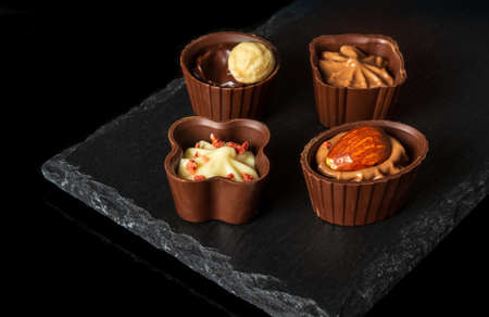 Chocolates with cream and nuts on a slate sorting board. Assorted chocolate on black isolated...