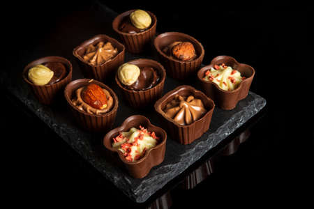 Candy with cream and nuts on a slate board. Assorted chocolate on black isolated background. Idea...