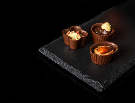 Chocolates with cream and nuts on a slate sorting board. Assorted chocolate on black isolated backgroundの写真素材