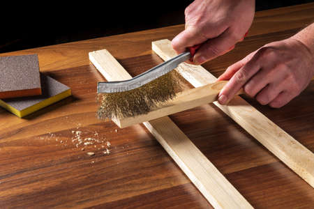 The craftsman cleans the wood plank with an abrasive tool. Builder hands close up. Renovation or construction ideaの写真素材