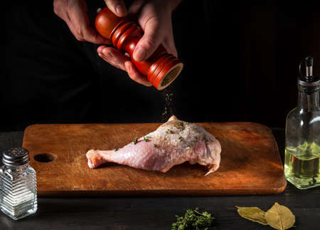 Cooking a chicken leg with the hands of a chef on a dark background. Add pepper to chicken meat....