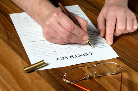 Drawing up contract in a working environment on the desktop. Close-up of man hands filling out blank...