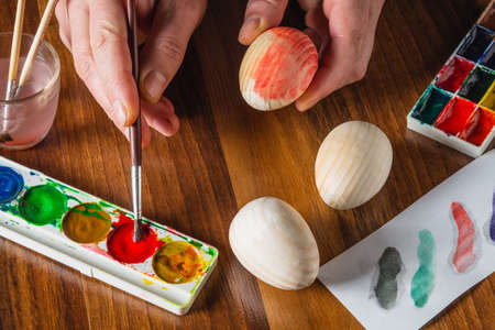 Hands of person decorate and paint easter eggs in different color on wooden table. Traditional and holiday fun. Top viewの写真素材