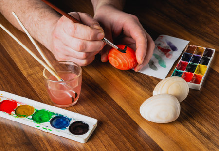 Human hands make brush strokes with watercolors on wooden eggs. Traditional and festive entertainment before Easter. View from aboveの写真素材