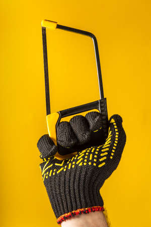Worker hand in glove holds saw or hacksaw on a yellow background. Idea for building or renovationの写真素材