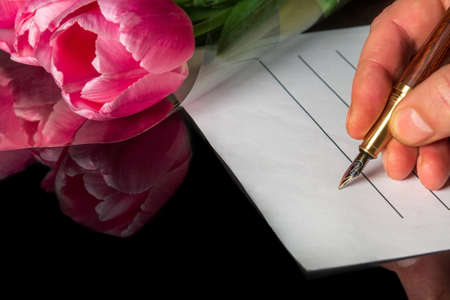 Stylish pen in the hand of a man on a blank sheet of paper and flowers in transparent packaging in...