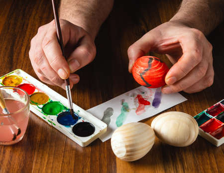 Person hands make brush strokes with watercolors on wooden eggs. Traditional and festive entertainment before Easter. Top viewの写真素材