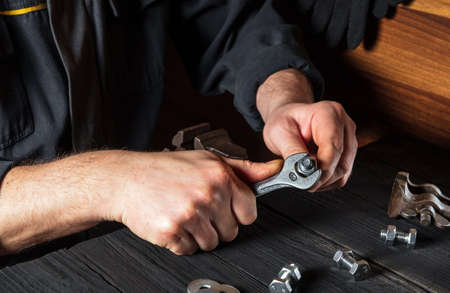 A craftsman tightens a nut with a wrench on a close-up of a bolt in a workshopの写真素材
