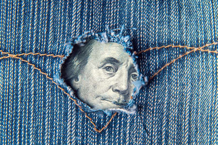 A hole in the pocket of denim pants from which dollars are visible. Symbolizes a crisis or a hole in the economy. Fall in profitsの写真素材