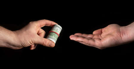 Person hand gives dollars and other human hand takes on black isolated background. The idea of bribery and corruptionの写真素材