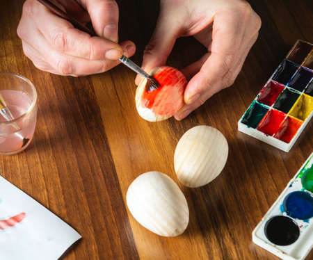 Person hands make brush strokes with watercolors on wooden eggs. Traditional and festive entertainment before Easterの写真素材