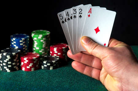 Poker cards with the high card or senior ace combination. Close-up of a gambler hand is holding playing cards in casino. Chips on the green tableの写真素材