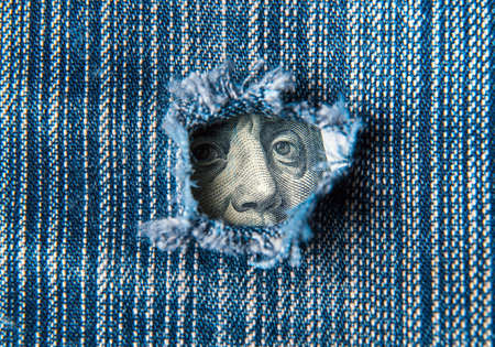 Hole in the pocket of denim pants from which dollars are visible. Symbolizes crisis or a hole in the economy. Falling financial profitの写真素材