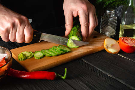Chef cutting a green cucumber in kitchen in the restaurant. Making a delicious salad with fresh vegetablesの写真素材