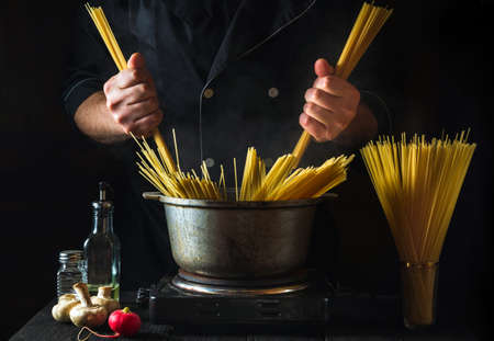 Chef cooks Italian pasta, on the background of vegetables. Close-up of a cook hand holding spaghetti in a restaurant kitchenの写真素材