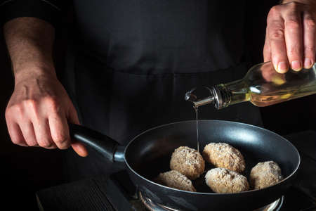 Cooking beef cutlets in a grill pan with the hands of a chef on a black background for copying the...