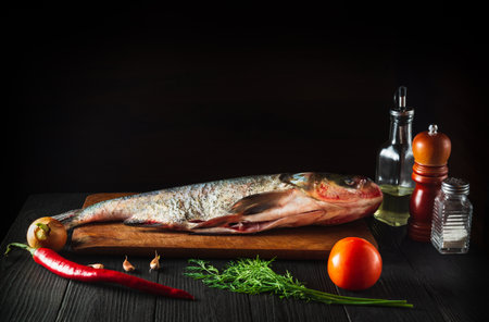Hypophthalmichthys or bighead carp on a cutting board with vegetables before cooking. Raw peeled...