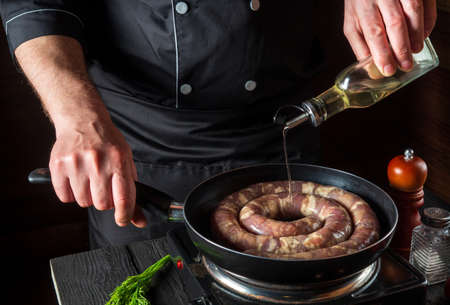 The chef adds oil to pan with raw meat sausage. Preparation for cooking sausages in the kitchen of a restaurant or cafe on a table with vegetablesの写真素材