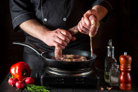 The chef holds the raw meat sausage before cooking. Working environment in a restaurant kitchen with...