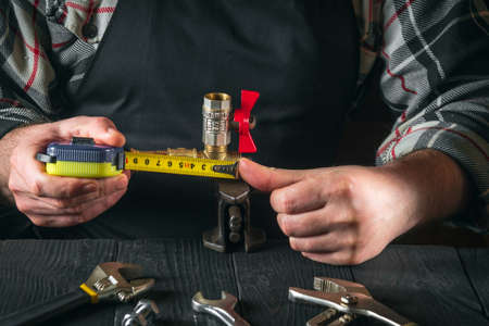 Master plumber measures the distance using a tape measure. Working environment in a workshop with...