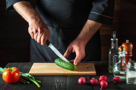 Professional chef or cook cuts green cucumber on restaurant kitchen table for salad. Vegetable diet or snack idea.の写真素材