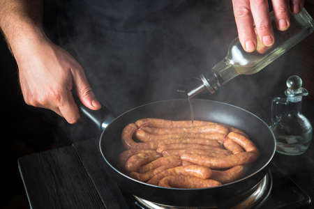The chef adds oil to pan with raw Munich sausages. Preparation for cooking sausages in the kitchen...
