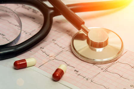 A medical stethoscope lies on a cardiogram chart and a pill close-up. Medical care, prevention, disease prevention or insurance concept. Cardiac care, health, protection and preventionの写真素材
