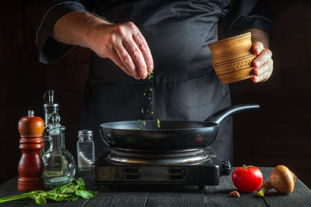 Professional chef or cook pours spices into pan. Frozen motion. Concept cooking process in the restaurant kitchenの写真素材