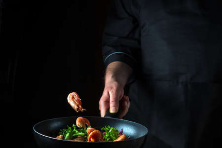 Professional chef or cook cooks shrimp in a pan with vegetables. Cooking seafood, healthy vegetarian...