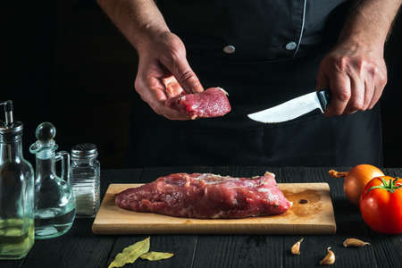 Chef or cook cutting beef meat with knife on kitchen, cooking food. Vegetables and spices on kitchen table to prepare delicious lunchの写真素材