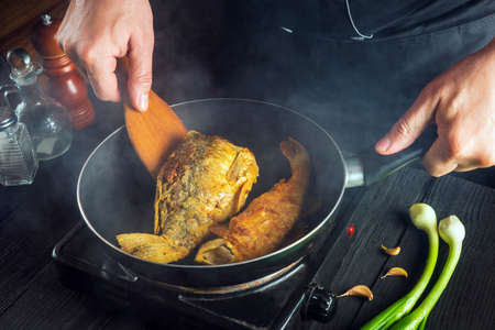 The chef prepares fish in the restaurant kitchen. Boil or fry crucian carp in a pan. The idea of a delicious fish diet.の写真素材