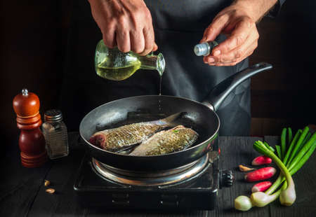 Professional chef prepares fresh fish in a pan with oil. Preparation for cooking fish food. Working environment in the kitchen of a restaurant or cafe.の写真素材
