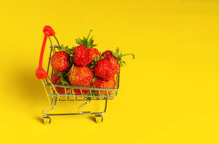 Fresh strawberries in a cart on a yellow background. Happy shopping concept. Free ad space.
